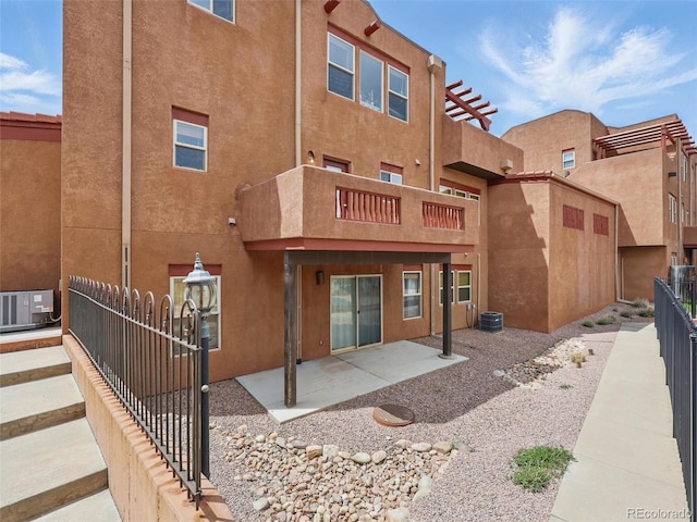 back of house with stucco siding, a balcony, fence, and cooling unit