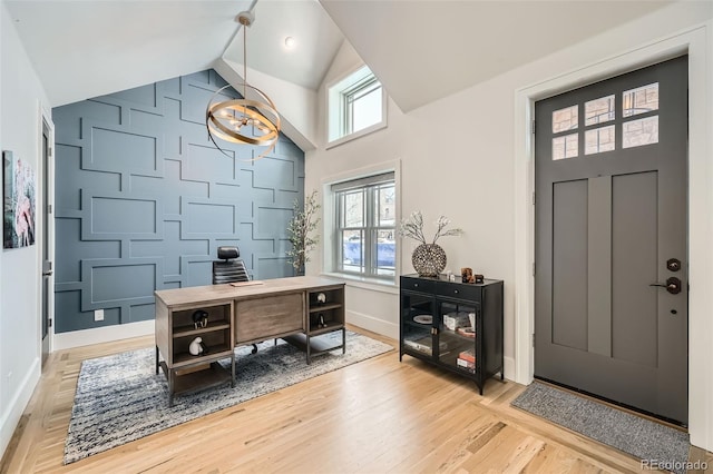 office area featuring light wood finished floors, a decorative wall, an accent wall, vaulted ceiling, and baseboards