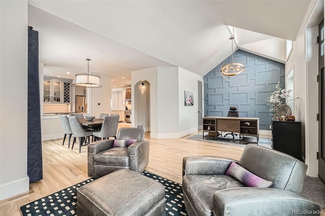 living area with vaulted ceiling, arched walkways, light wood-style flooring, and baseboards