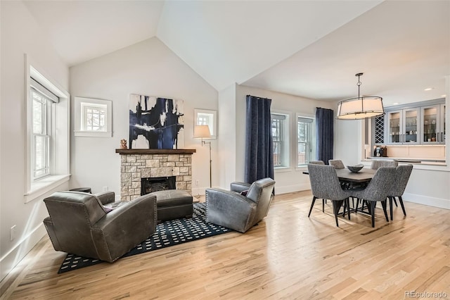 living area with light wood-type flooring, baseboards, vaulted ceiling, and a stone fireplace