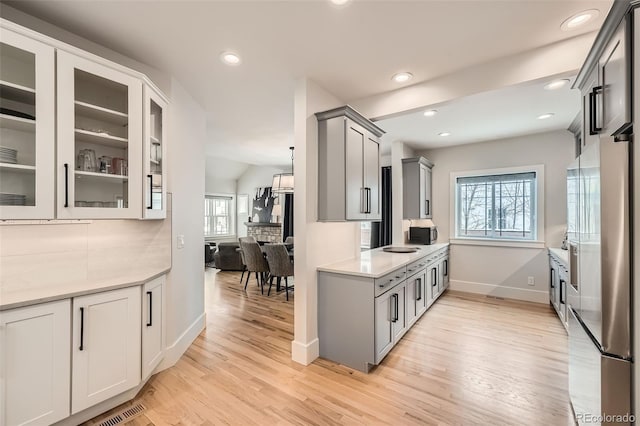 kitchen featuring gray cabinetry, light wood-style floors, light countertops, freestanding refrigerator, and glass insert cabinets