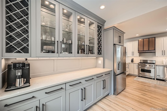 kitchen featuring glass insert cabinets, gray cabinets, stainless steel appliances, light wood-type flooring, and recessed lighting