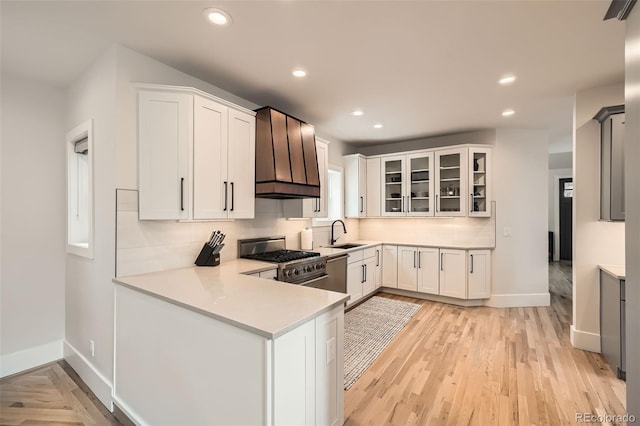 kitchen with a sink, white cabinets, light countertops, high end stainless steel range oven, and glass insert cabinets