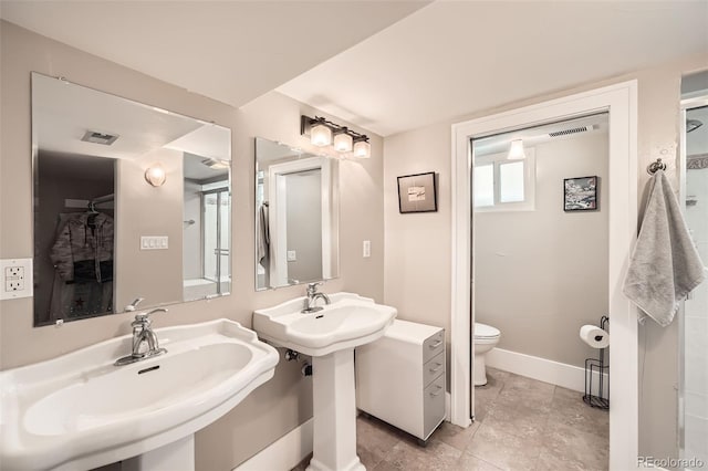 bathroom featuring baseboards, two sinks, visible vents, and toilet