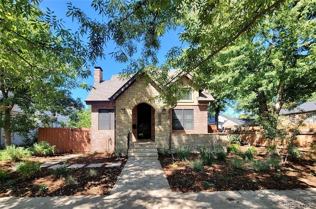 view of front of home with stone siding, brick siding, a chimney, and fence