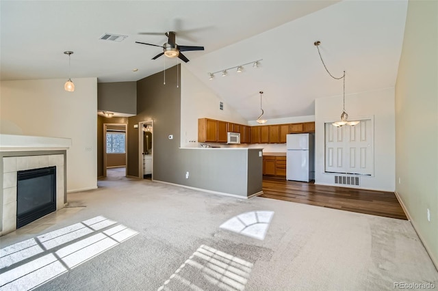 unfurnished living room with a tiled fireplace, light colored carpet, track lighting, and high vaulted ceiling