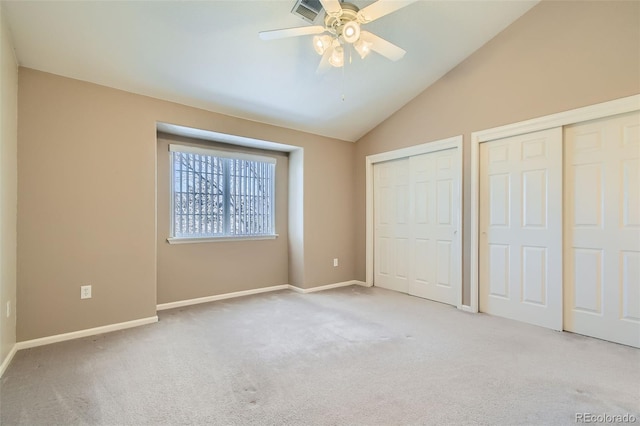 unfurnished bedroom featuring light carpet, multiple closets, vaulted ceiling, and ceiling fan