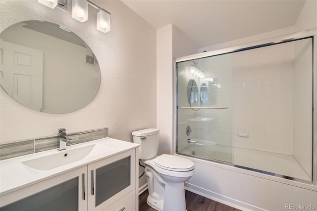 full bath featuring bath / shower combo with glass door, a textured wall, toilet, vanity, and wood finished floors