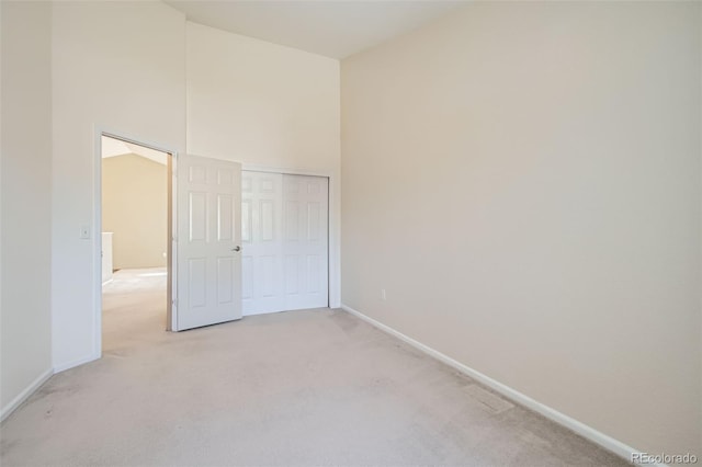 unfurnished bedroom with a high ceiling, baseboards, a closet, and light colored carpet