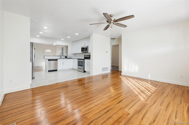 unfurnished living room featuring recessed lighting, light wood-style flooring, a ceiling fan, a sink, and baseboards