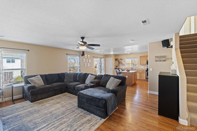 living area featuring baseboards, a ceiling fan, stairs, a textured ceiling, and light wood-type flooring