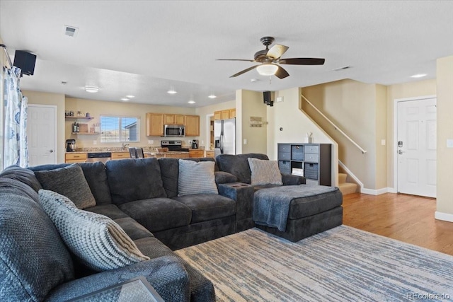 living area with visible vents, stairway, light wood-style floors, a ceiling fan, and baseboards