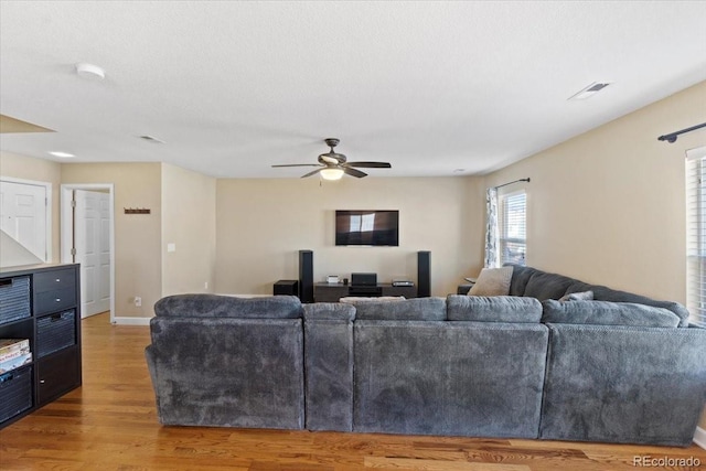 living room with a ceiling fan, visible vents, baseboards, and wood finished floors