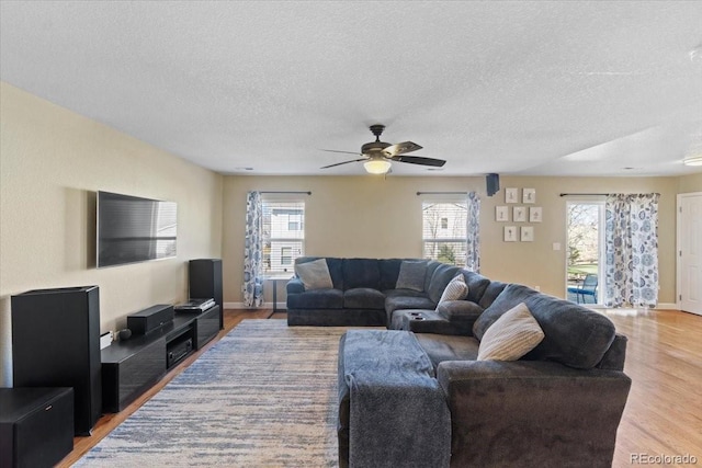 living room featuring light wood-style floors, plenty of natural light, a textured ceiling, and a ceiling fan