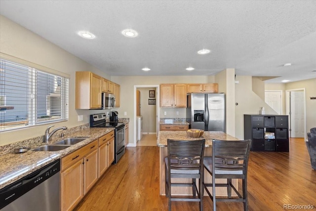 kitchen with appliances with stainless steel finishes, a sink, a breakfast bar area, and wood finished floors