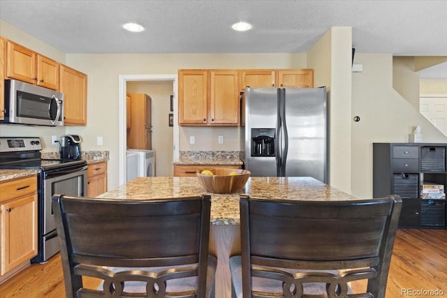 kitchen featuring stainless steel appliances, light wood-type flooring, a kitchen island, and light stone countertops