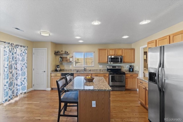 kitchen with a kitchen island, a sink, a kitchen breakfast bar, appliances with stainless steel finishes, and light wood finished floors