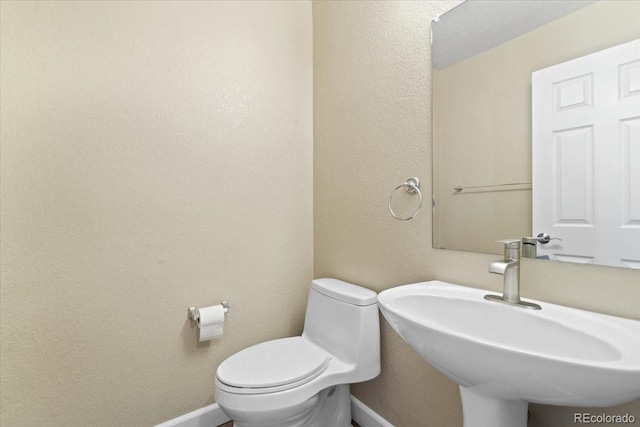 half bath featuring a sink, toilet, and baseboards