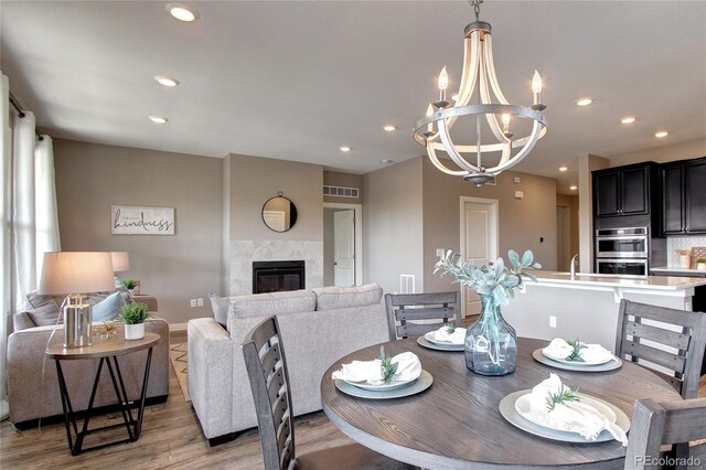 4090 Forever Cir, Castle Rock, CO 80109 - dining area with light wood finished floors, a chandelier, a glass covered fireplace, recessed lighting, and baseboards