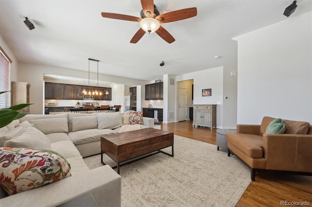 living room with ceiling fan with notable chandelier and hardwood / wood-style floors