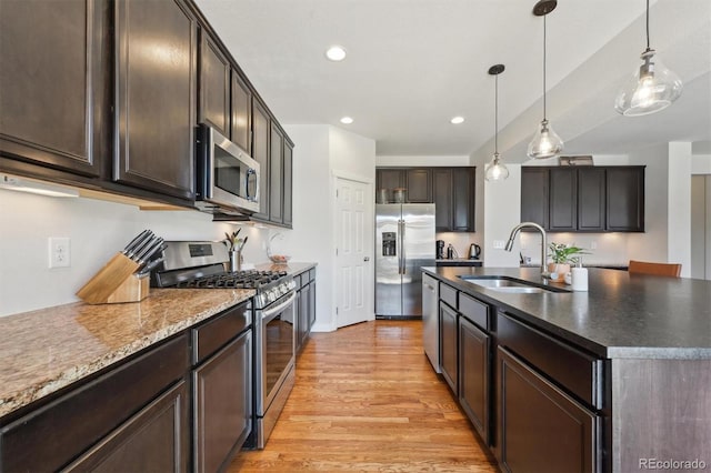 kitchen featuring dark brown cabinetry, sink, hanging light fixtures, appliances with stainless steel finishes, and a kitchen island with sink