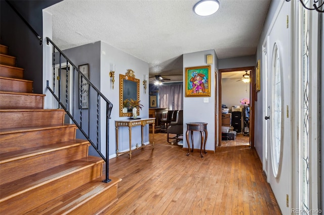 entrance foyer featuring light wood-type flooring, ceiling fan, stairway, and a textured ceiling