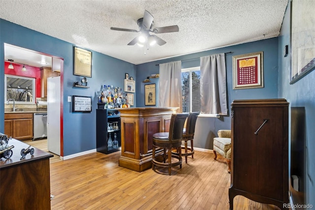 bar with light wood finished floors, a ceiling fan, a bar, dishwasher, and baseboards