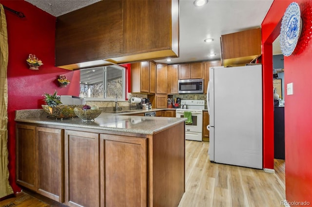 kitchen featuring a peninsula, white appliances, a sink, light wood-style floors, and brown cabinets