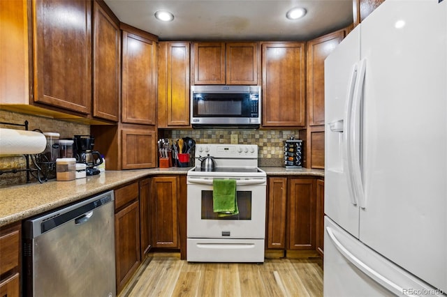 kitchen with appliances with stainless steel finishes, brown cabinets, light wood-style flooring, and backsplash