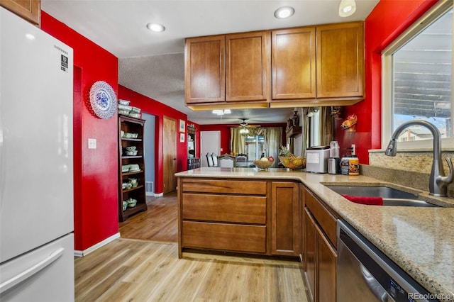 kitchen with dishwasher, brown cabinets, freestanding refrigerator, light wood-style floors, and a sink