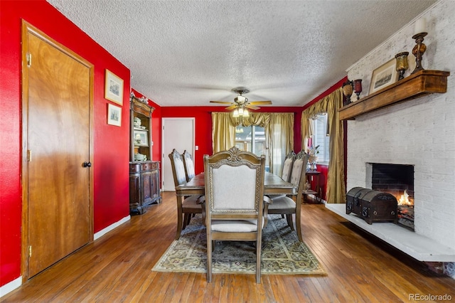 dining space with hardwood / wood-style floors, a ceiling fan, a brick fireplace, a textured ceiling, and baseboards