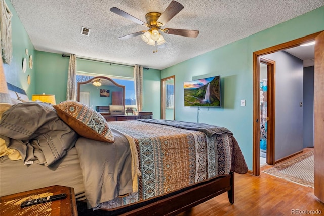 bedroom featuring a ceiling fan, visible vents, a textured ceiling, and wood finished floors