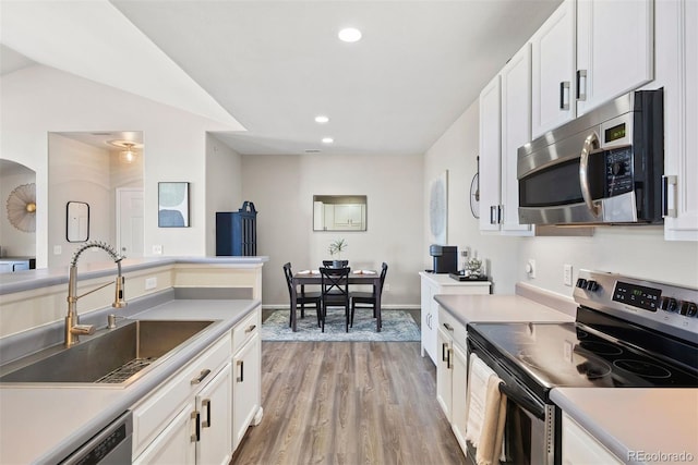 kitchen with stainless steel appliances, white cabinets, a sink, and light wood finished floors