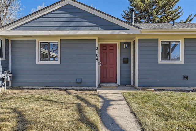 view of exterior entry featuring a lawn and roof with shingles