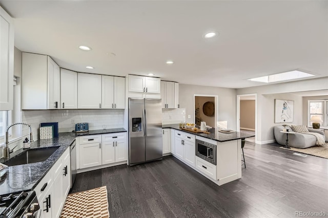 kitchen featuring a peninsula, dark wood-type flooring, a skylight, a sink, and appliances with stainless steel finishes