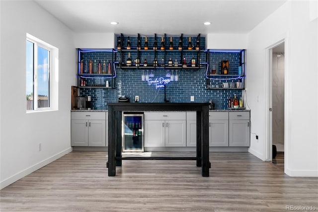 bar featuring light hardwood / wood-style flooring, backsplash, dark stone countertops, wine cooler, and white cabinets