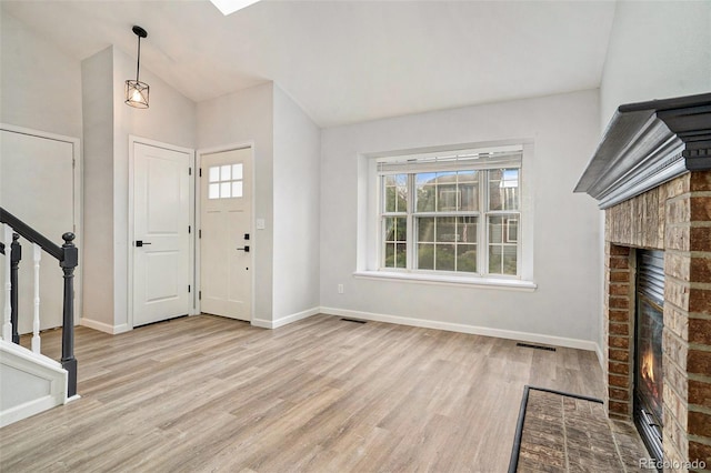 foyer with light hardwood / wood-style flooring, a brick fireplace, and lofted ceiling