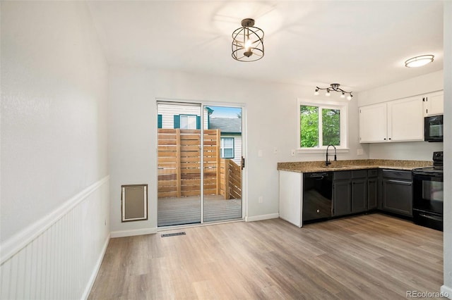 kitchen with pendant lighting, white cabinets, black appliances, sink, and light wood-type flooring