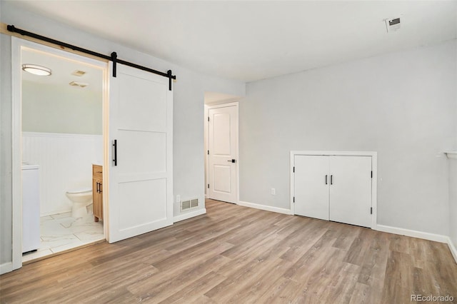 unfurnished bedroom featuring a barn door, a closet, ensuite bath, and light hardwood / wood-style flooring