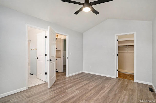 unfurnished bedroom featuring lofted ceiling, ensuite bathroom, ceiling fan, a spacious closet, and a closet