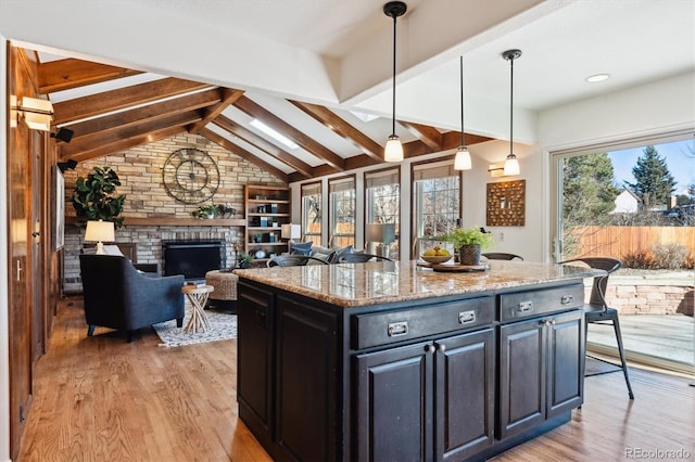 kitchen featuring light stone countertops, light hardwood / wood-style flooring, hanging light fixtures, a center island, and vaulted ceiling with beams