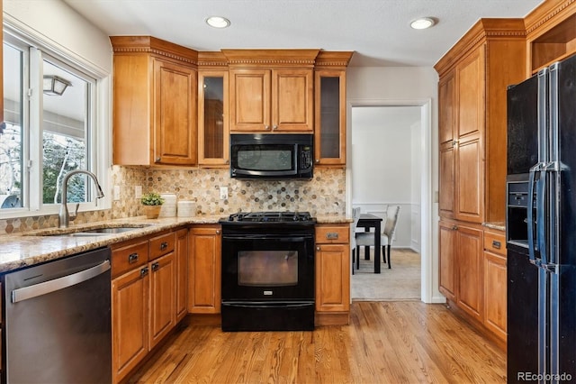 kitchen with light stone countertops, light hardwood / wood-style flooring, black appliances, tasteful backsplash, and sink