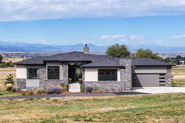 prairie-style house featuring an attached garage, a front lawn, concrete driveway, stone siding, and a mountain view