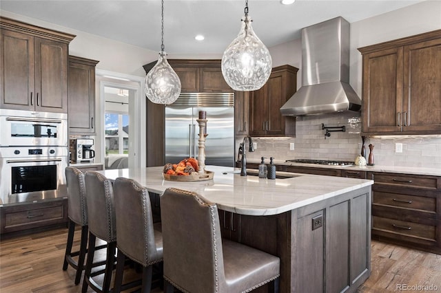 kitchen with wall chimney range hood, tasteful backsplash, dark wood-style flooring, and appliances with stainless steel finishes