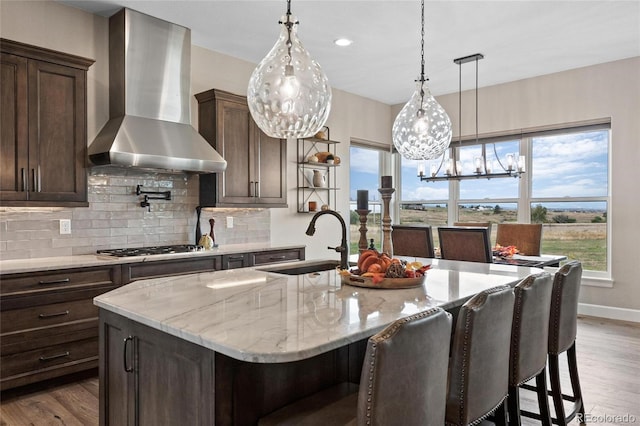 kitchen featuring dark wood-type flooring, wall chimney range hood, stainless steel gas cooktop, and a sink