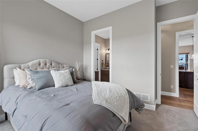 bedroom featuring visible vents, baseboards, light carpet, ensuite bathroom, and a sink