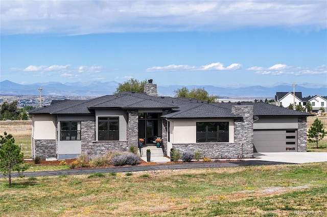 prairie-style home featuring a front lawn, stone siding, a mountain view, concrete driveway, and a garage