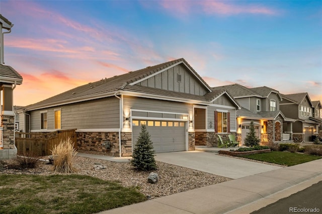 craftsman-style house featuring concrete driveway, board and batten siding, stone siding, an attached garage, and a tile roof