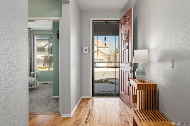 doorway featuring baseboards, light wood finished floors, and a textured wall