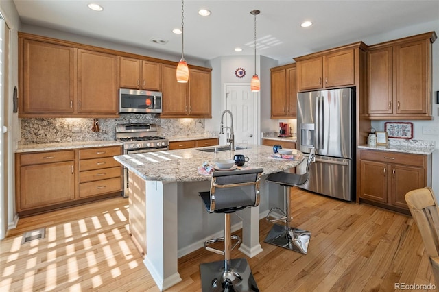 kitchen with light wood-style floors, brown cabinetry, tasteful backsplash, a sink, and stainless steel appliances